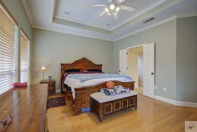 bedroom with a tray ceiling, visible vents, baseboards, and light wood-style floors