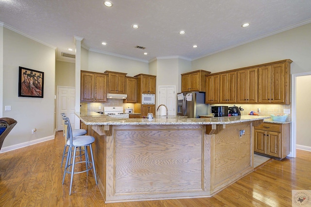 kitchen featuring under cabinet range hood, white appliances, a breakfast bar, and brown cabinetry