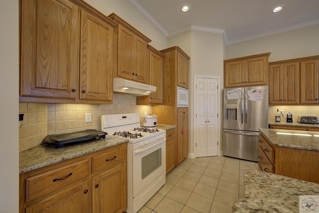 kitchen with white appliances, light tile patterned floors, brown cabinets, and under cabinet range hood