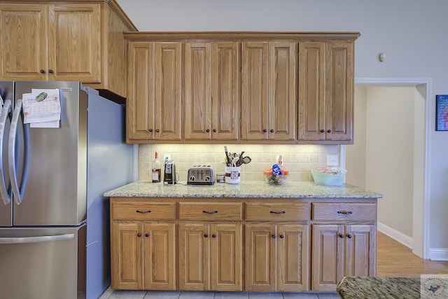 kitchen featuring light stone counters, decorative backsplash, brown cabinetry, and freestanding refrigerator