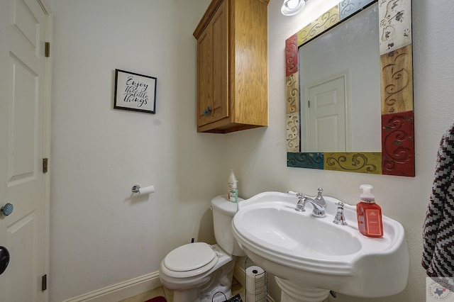 half bath with toilet, baseboards, and a sink