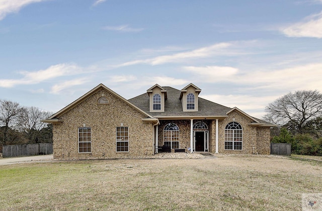 view of front facade with a front yard, fence, brick siding, and roof with shingles