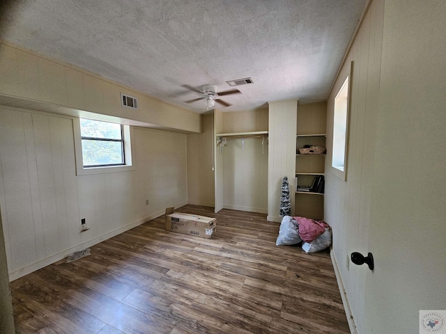 unfurnished bedroom featuring a textured ceiling, wooden walls, ceiling fan, and dark hardwood / wood-style flooring