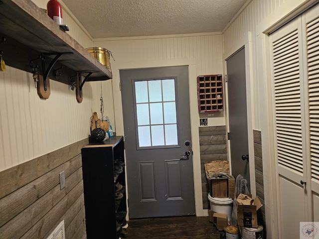 doorway to outside featuring wood walls, crown molding, dark wood-type flooring, and a textured ceiling