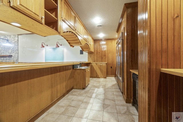 kitchen with built in refrigerator, wood walls, brown cabinetry, and light countertops