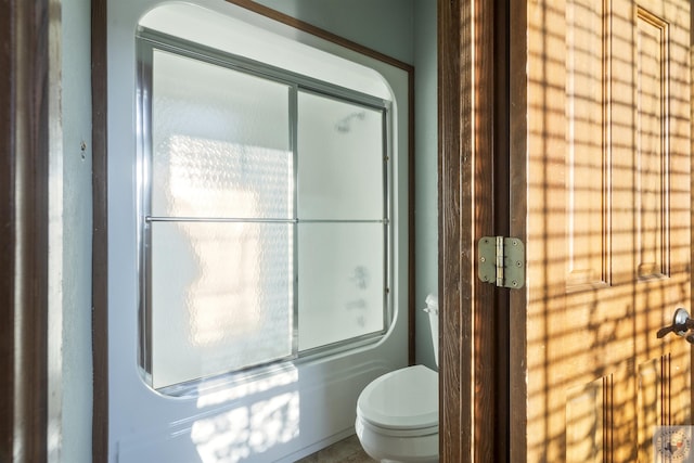 bathroom featuring toilet and shower / bath combination with glass door