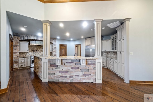 kitchen featuring stainless steel built in refrigerator, a kitchen breakfast bar, tasteful backsplash, decorative columns, and light stone countertops