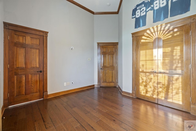 empty room featuring baseboards, a high ceiling, dark wood-style flooring, and crown molding