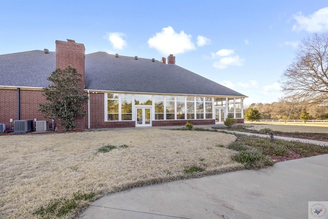 back of property featuring brick siding, central AC, french doors, a chimney, and a sunroom