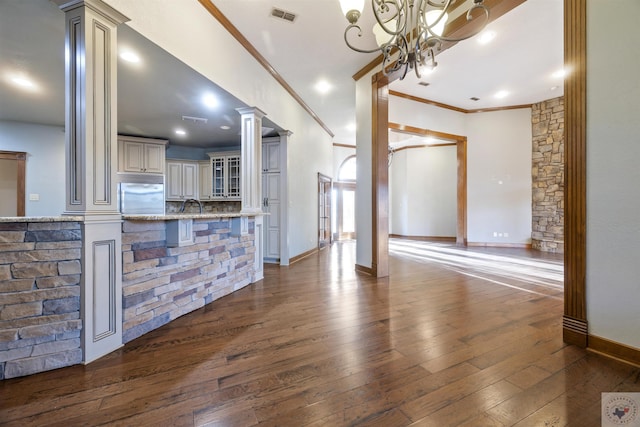 unfurnished living room with baseboards, visible vents, ornate columns, a sink, and dark wood-type flooring