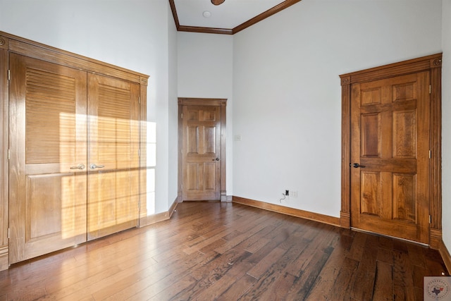 unfurnished bedroom with a high ceiling, dark wood-type flooring, baseboards, and ornamental molding