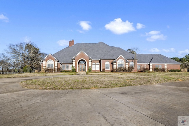 view of front of property with a front yard, brick siding, roof with shingles, and a chimney