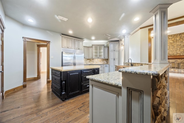 kitchen with stainless steel built in refrigerator, a kitchen island, hardwood / wood-style floors, dark cabinetry, and decorative backsplash