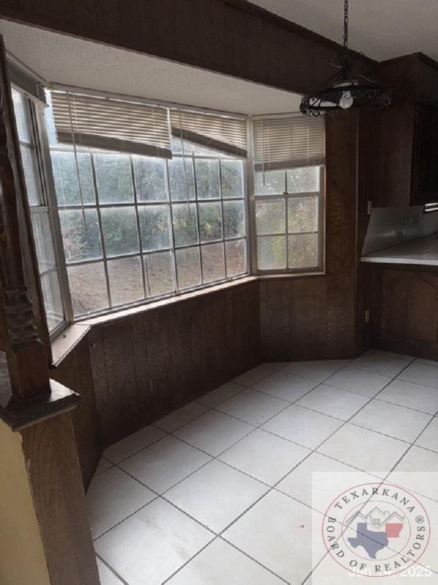 unfurnished dining area featuring light tile patterned flooring and wooden walls