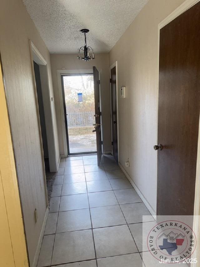 doorway to outside with a textured ceiling, light tile patterned floors, and a notable chandelier