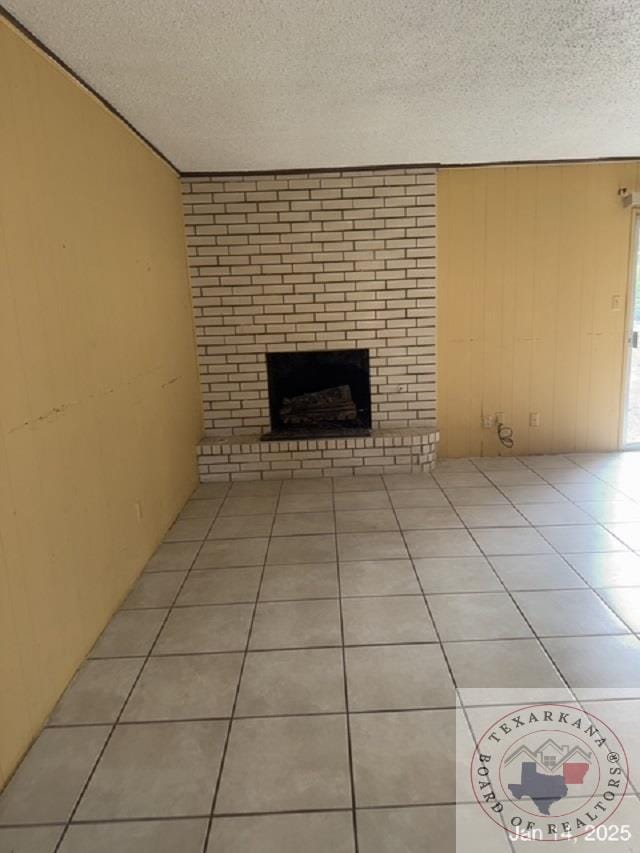 unfurnished living room with a textured ceiling, light tile patterned floors, and a brick fireplace