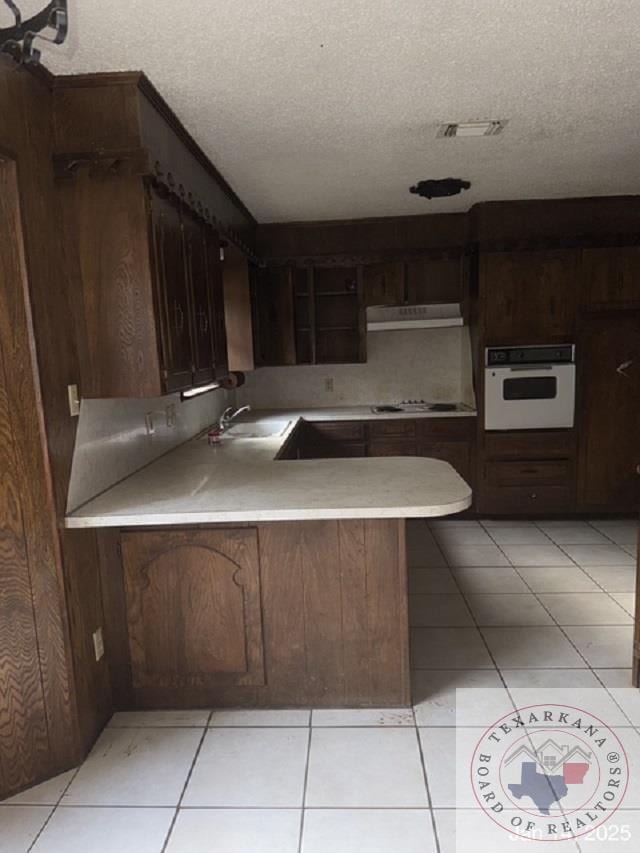 kitchen with a textured ceiling, dark brown cabinets, sink, kitchen peninsula, and white oven