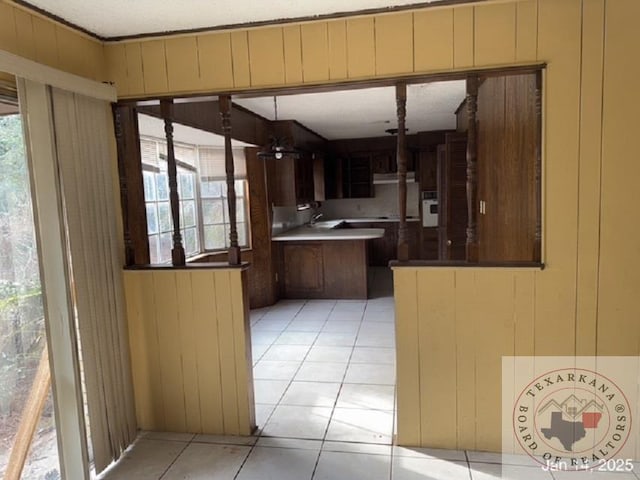 kitchen featuring dark brown cabinets, a healthy amount of sunlight, wooden walls, and light tile patterned floors