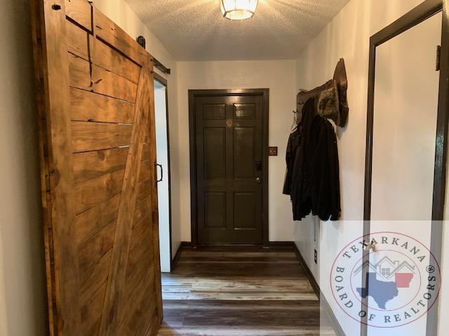 doorway to outside with a barn door, dark wood-type flooring, and a textured ceiling