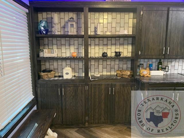 bar with wood-type flooring, tasteful backsplash, and dark brown cabinetry