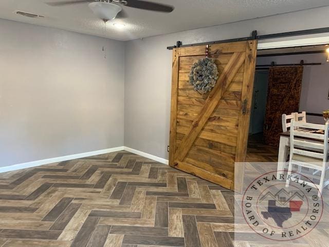 unfurnished room with ceiling fan, a textured ceiling, dark parquet floors, and a barn door