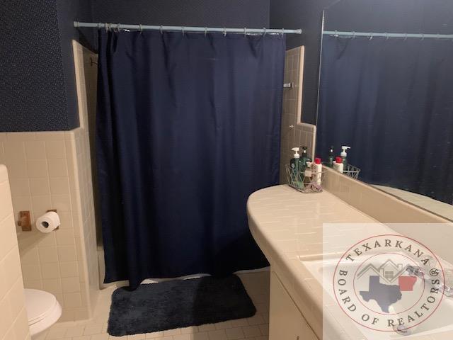 full bathroom with tile patterned floors, vanity, tile walls, toilet, and shower / tub combo with curtain