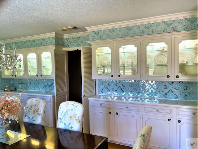 501 Park St, Atlanta, TX 75551 - kitchen with a textured ceiling, visible vents, ornamental molding, glass insert cabinets, and wallpapered walls