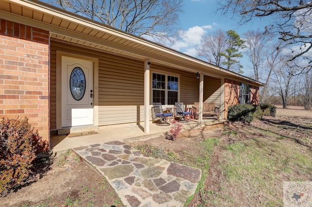 property entrance with covered porch, a patio, and brick siding