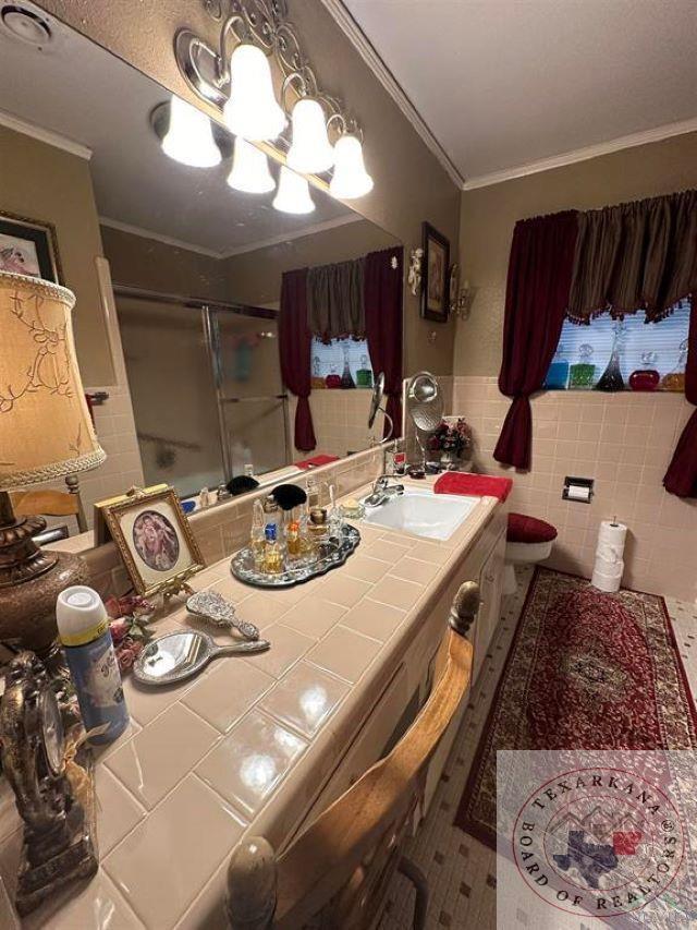 bathroom featuring toilet, an enclosed shower, tile walls, ornamental molding, and vanity