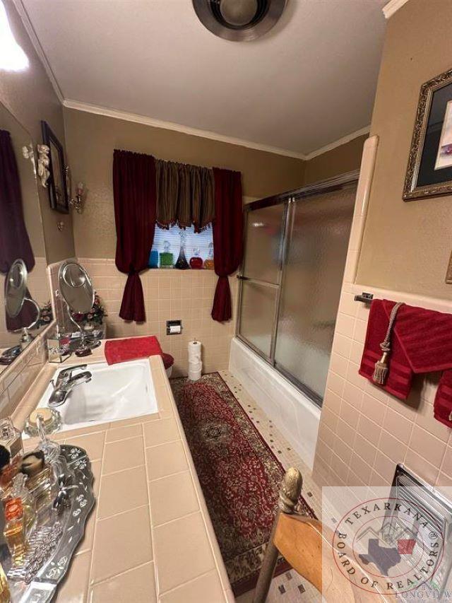 bathroom with tile patterned flooring, vanity, bath / shower combo with glass door, tile walls, and ornamental molding