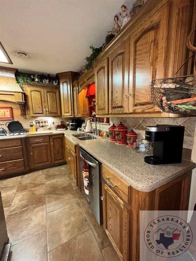 kitchen featuring light stone countertops, dishwasher, sink, backsplash, and light tile patterned floors