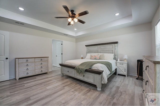 bedroom featuring ceiling fan, light hardwood / wood-style floors, and a tray ceiling