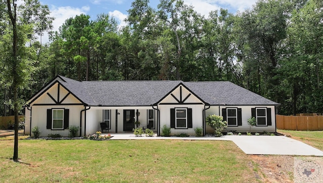 tudor house with a shingled roof, fence, a front lawn, and a patio