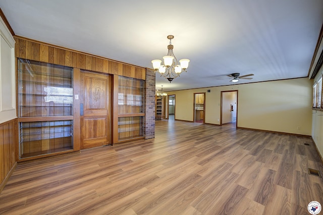 empty room with visible vents, wood walls, wood finished floors, ceiling fan with notable chandelier, and a wealth of natural light