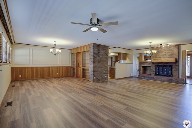 unfurnished living room featuring visible vents, a brick fireplace, wood finished floors, baseboards, and ceiling fan with notable chandelier
