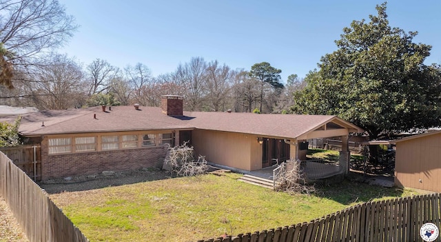 back of house featuring a lawn, a fenced backyard, a chimney, and brick siding