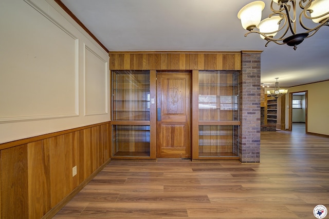 interior space with an inviting chandelier, wood walls, crown molding, and wood finished floors