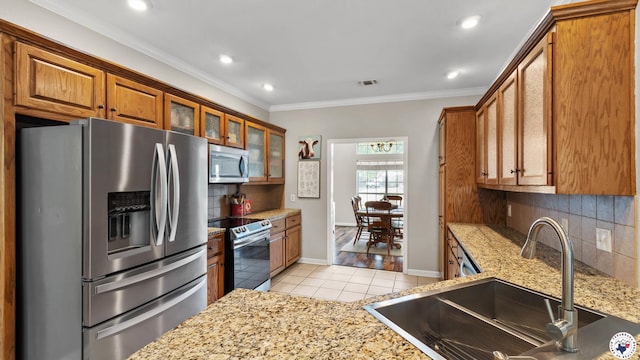 kitchen with brown cabinetry, light tile patterned floors, a sink, backsplash, and stainless steel appliances