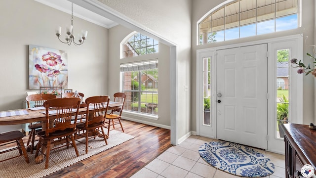 foyer entrance featuring a towering ceiling, crown molding, baseboards, a chandelier, and light wood-style flooring