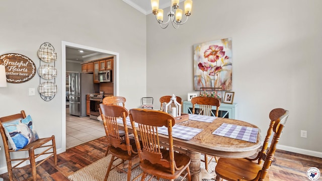 dining area with crown molding, baseboards, a chandelier, a high ceiling, and light wood-style flooring