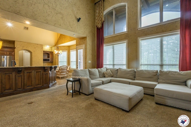 living area featuring visible vents, a notable chandelier, high vaulted ceiling, and light colored carpet