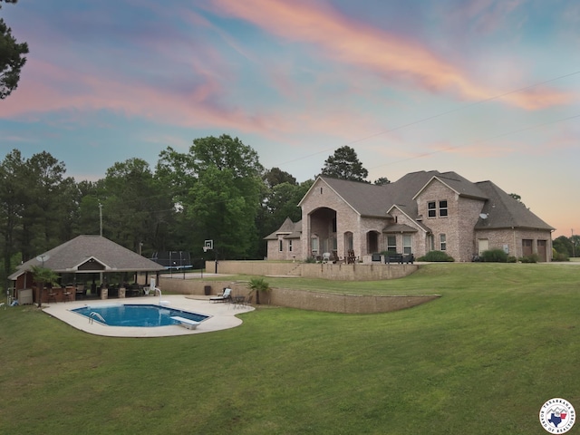 back of house featuring brick siding, stone siding, a fenced in pool, a patio, and a yard
