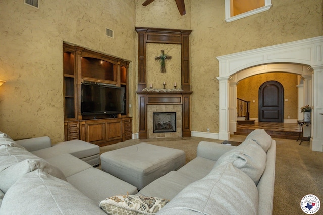living area featuring a high ceiling, arched walkways, a tile fireplace, ornate columns, and visible vents