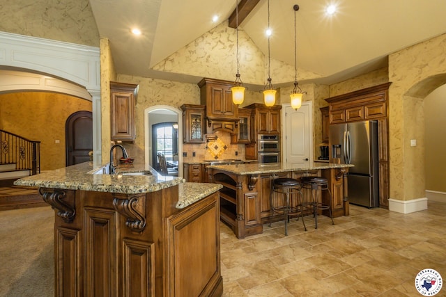 kitchen featuring appliances with stainless steel finishes, a breakfast bar, beam ceiling, a sink, and arched walkways
