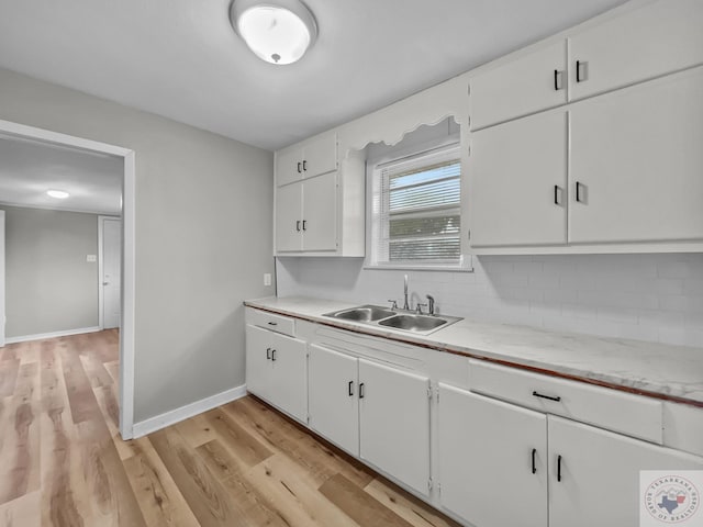 kitchen featuring sink, light wood-type flooring, white cabinetry, and tasteful backsplash