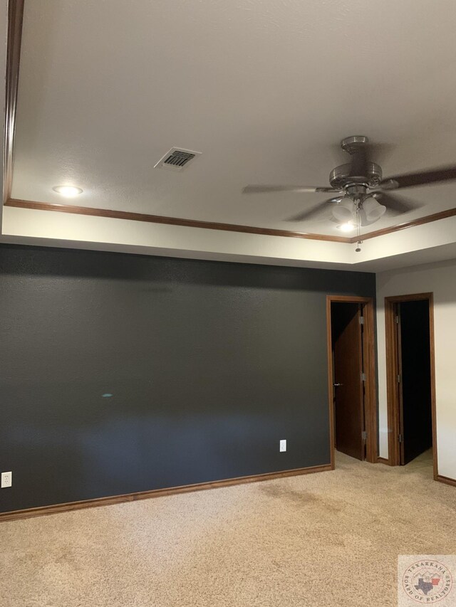 empty room featuring ceiling fan, light colored carpet, and a tray ceiling