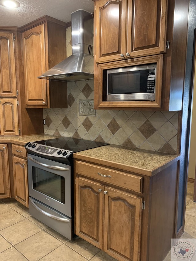 kitchen with appliances with stainless steel finishes, tasteful backsplash, a textured ceiling, light tile patterned floors, and wall chimney range hood