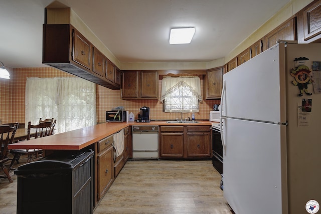 kitchen with light countertops, a sink, white appliances, a peninsula, and light wood-style flooring