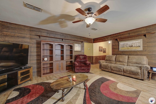 living area featuring ceiling fan, visible vents, wood finished floors, and wooden walls
