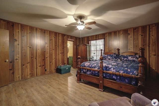 bedroom with wooden walls, light wood-type flooring, and ceiling fan